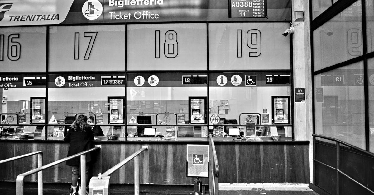 Monochrome image of a train station ticket office with numbered counters, showcasing travel services.